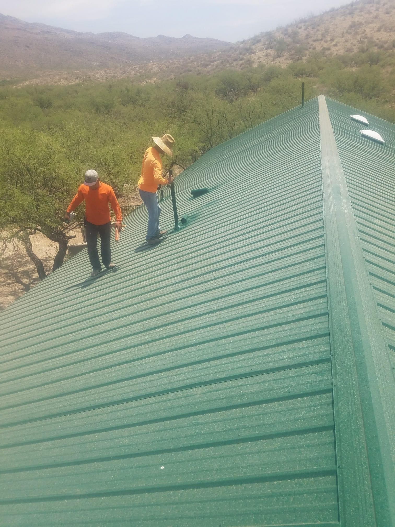 Coronado Roofing crew installing standing-seam metal panels on a forest-green roof in the Tucson high desert