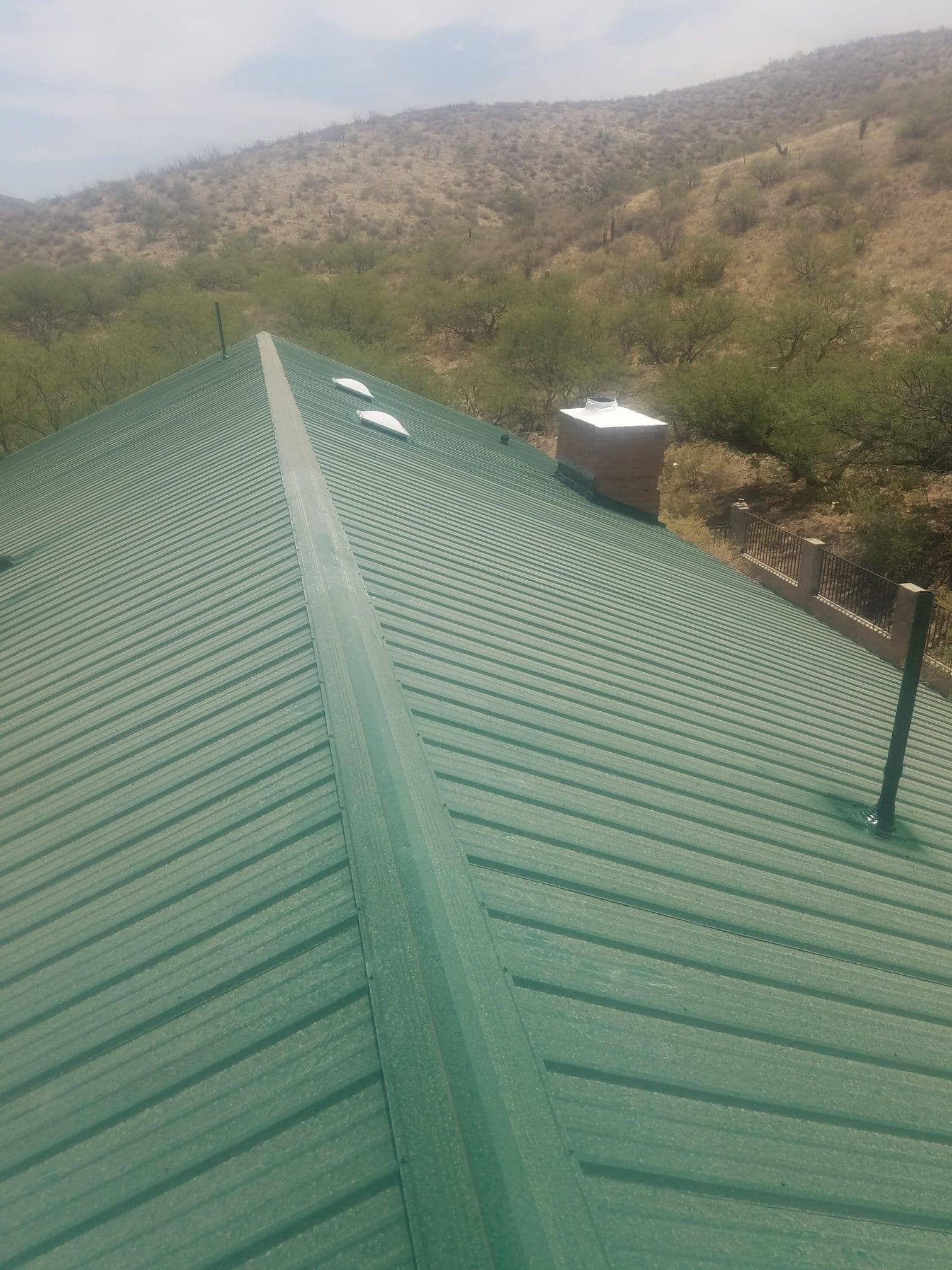 Finished forest-green standing-seam metal roof on a Tucson-area home, looking down the ridge with desert mountains behind